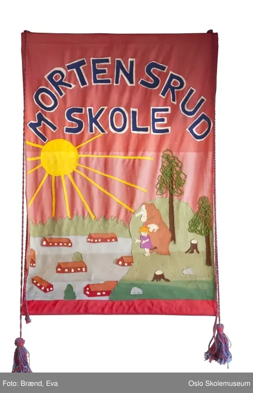 Nyere fane: Landskap med skolens egne bygninger og skogen rundt på blå bakgrunn. Stiliserte barn og dyr samte en stor gul sol. Øverst på fanen står skolens navn. 

Eldre fane: Landskap med skolens egene bygninger og skogen rundt på rød bakgrunn. Stil og formspråk hentet fra folkeeventyrene. Øverst på fanen står skolens navn.