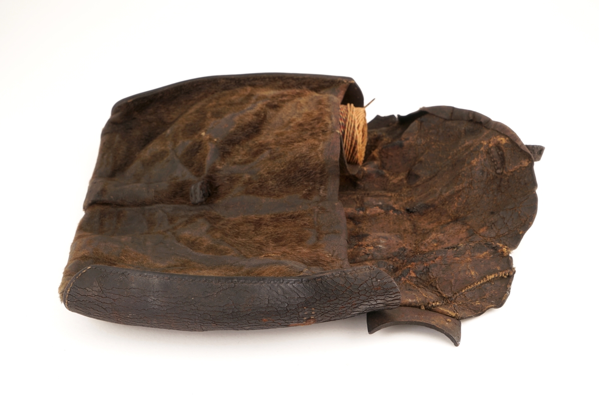 Veske av selskinn hvor det på lokket er festet en lærrem med hull. På vesken er det rester etter antatt låseanordning for lærremmen på lokket. Hovedrom i vesken er delt i to med selskinn. i det ene rommet er det en rull med rød/blå/hvit tråd av bomull (plomberingstråd). I det andre rommet ligger det tre blyplomber.