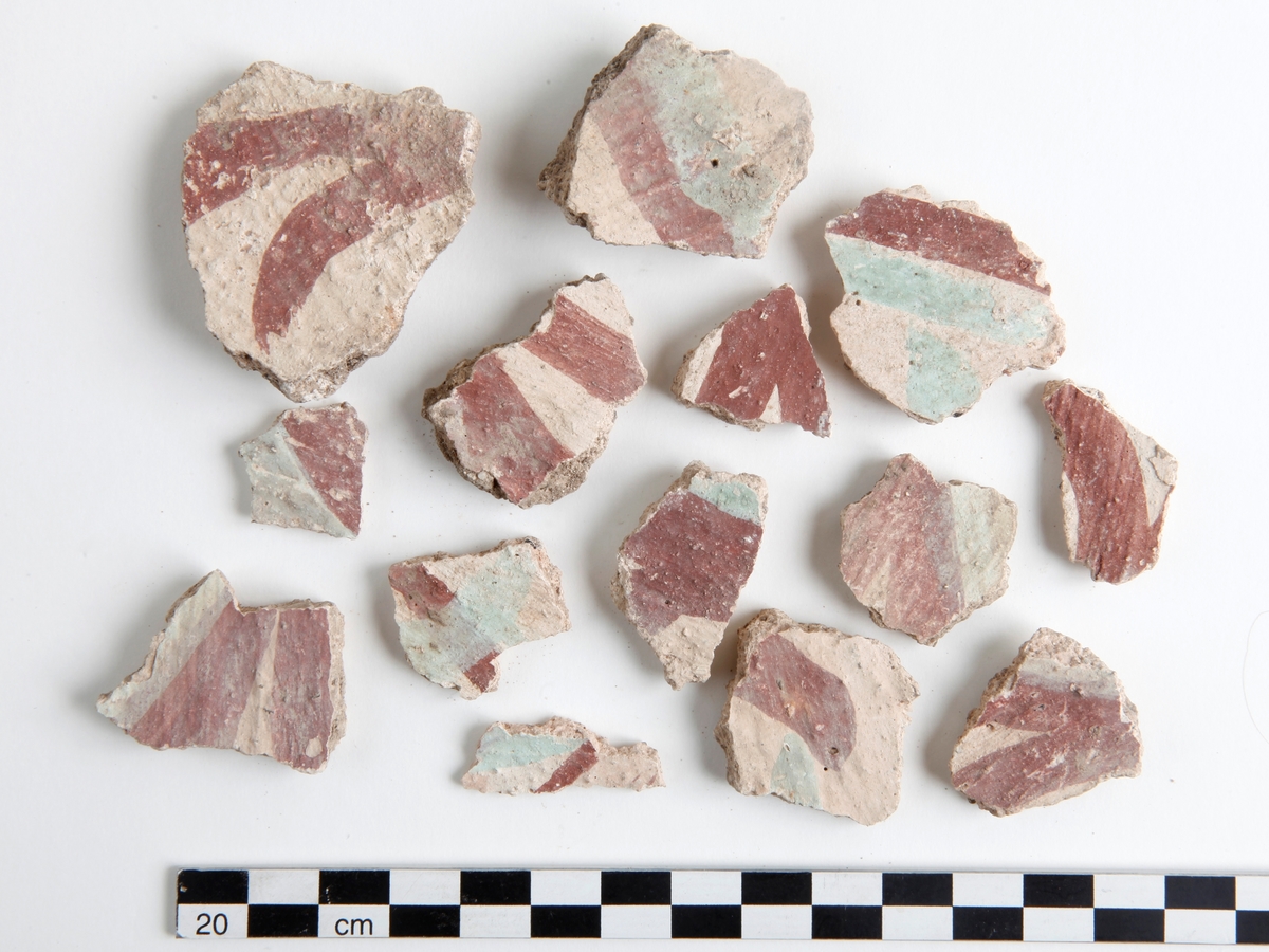 Fragment av kalkputs. Bemålade kalkputsfragment med schablonmotiv samt heltäckande färger i rött, grönt/turkos, gult, orange, svart, och brunt. Datering sent 1400-tal.