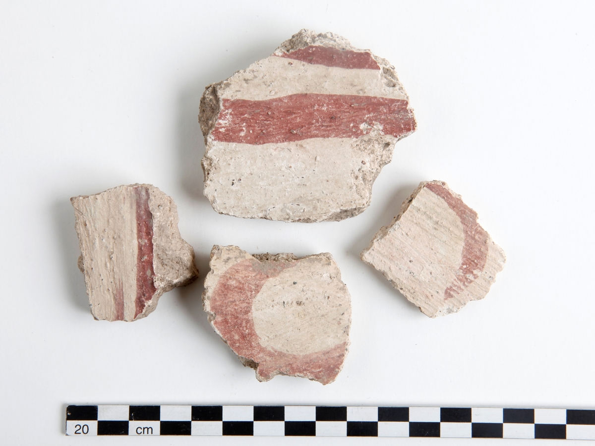 Fragment av kalkputs. Bemålade kalkputsfragment med schablonmotiv samt heltäckande färger i rött, grönt/turkos, gult, orange, svart, och brunt. Datering sent 1400-tal.