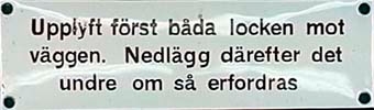 Rektangulär emaljerad skylt med brun text på vit botten:
       Upplyft först båda locken mot
       väggen. Nedlägg därefter det
       undre, om så erfordras.

Anm. Samma budskap har 11566-80. Stavn./avstavn. skiljer.