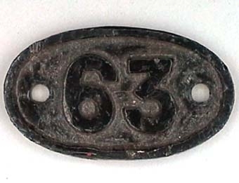 Oval skylt av svartmålad mässing med text i relief: "63".
Från ångloket EHRJ 3 
SWB 63 (1914)
SJ KA8 1686
NOHAB Nº 770.