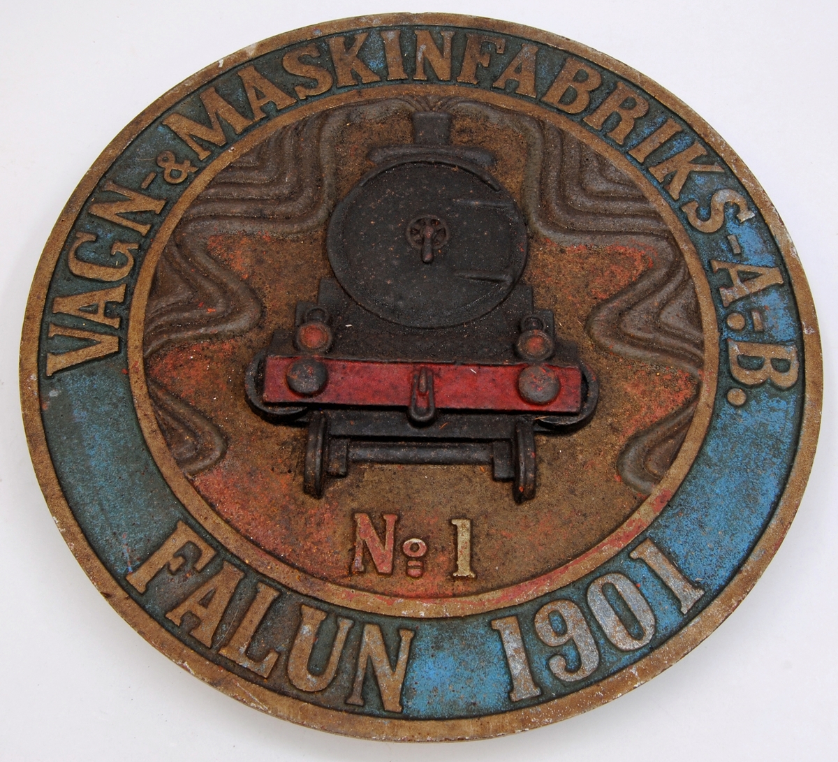Cirkelformad loktillverkarskylt. Kanten längst ut är gulfärgad och i relief. Efter kanten finns texten: "VAGN-&MASIKFABRIKS-A.B. FALUN 1901" i en guldfärg och i relief på ljusblå botten. Mitt på finns en guldfärgad cirkelformad linje i relief. I cirkelformen finns ett svart ånglok sett framifrån med ånga som kommer ut från skorstenen. Bilden är i relief och botten är röd. Under ångloket finns: "No 1" i guldfärg och relief. 

Historik: Skylten är troligtvis en kopia på skylt till ångloket Ka 693 (se Jvm 20818:1).