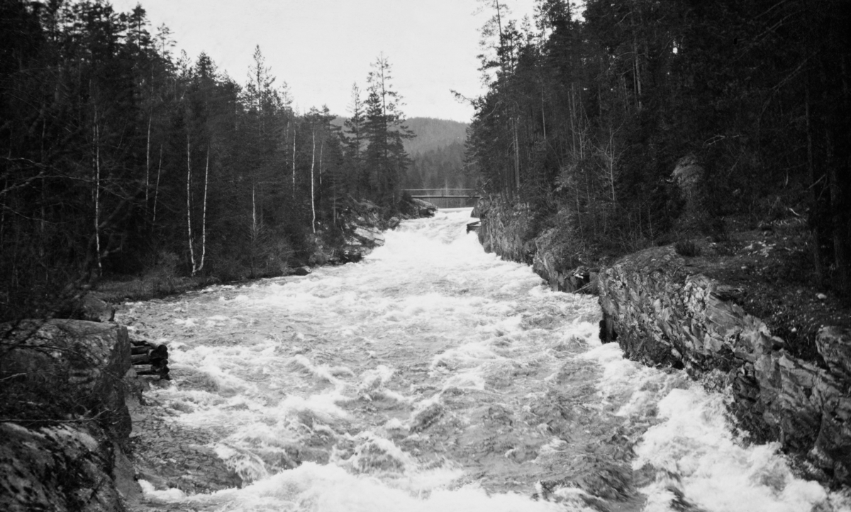 Fulldøla – et par kilometer langt eleveløp fra Follsjø til Tinnåa i Notodden kommune i Telemark. Fotografiet later til å være tatt fra ei bru oppover elveløpet, som her går stridt og stort i bergrikt lende, der det også er et par små fossefall.  Ved et av disse skimter vi en liten skådam på høyre side av elva og enda lengre oppe ser vi et bruspenn.  Fulldøla har et nedslagsfelt på 115 kvadratkilometer, og i dette området vokser det mye skog, så elva var ei viktig fløtingselv, sjøl om forholdene, som dette bildet viser, ikke var de beste.  Vanskelige fløtingsforhold ble kompensert ved regulering av Follsjå og bygging av ei 500 meter lang tømmerrenne.  Fotografiet er tatt i forbindelse med ei fløtingsbefaring sommeren 1921. Fløtinga i dette vassdraget var årviss fram til 1970.  Etter dette har det bare vært fløtet tømmer en sesong i Fulldøla. 

Jfr. SJF. 1989-02141