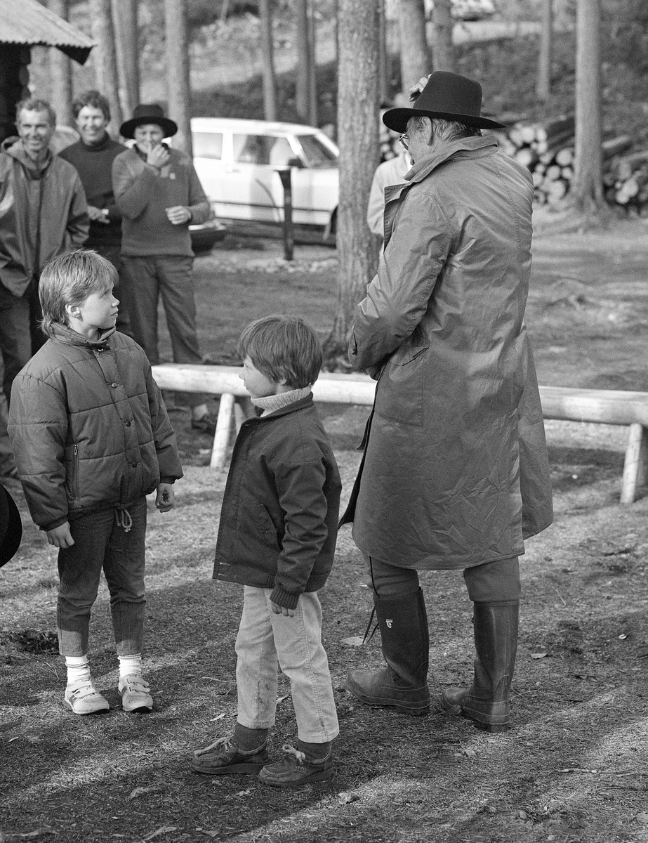 Fra Klarälvens Flottningsförenings styrebefaring langs den øvre delen av Trysilvassdraget i mai 1986.  På bildet ser vi forstmannen Ture Björkman, som hadde hatt flere sentrale roller i treforedlingskonsernet Billerud AB, som kjøpte tømmer fra Engerdal og Trysil.  Björkman var iført regnfrakk og hadde en ny, vidbremmet filthatt på hodet.  Hatten var sannsynligvis en gave alle gjestene fra fløtingsstyret i Karlstad fikk fra det lokale fløtermiljøet på norsk side.  Tanken bak gaven var sannsynligvis å stimulere til samhørighet mellom de sentrale aktørene i Värmlands skogindustri og fløterne som bidro til at de fikk norsk råstoff.  Fotografiet er fra Stenbekkoia ved Femundselva, der også mange av fløterne og deres familier var til stede.  To barn sto like ved Björkman da dette bildet ble tatt.  Litt biografisk informasjon finnes under fanen «Opplysninger».