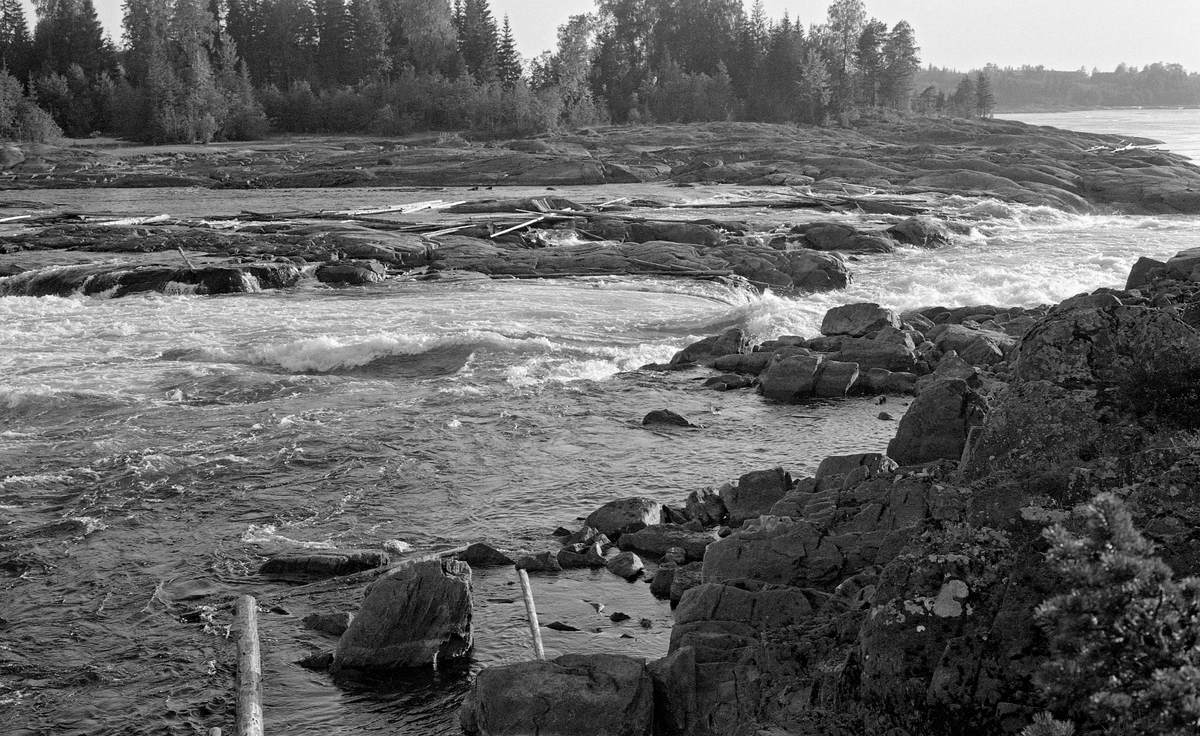 Fra Funnefossen i Nes i Akershus.  Fotografiet er tatt en seinsommerdag i 1959.  Funnefossen har et samlet fall på nesten 11 meter over en distanse på om lag 850 meter.  Der hvor dette fotografiet er tatt går elva over ei bergflate, der tømmeret hadde lett for å strande på oppstikkende svaberg ved lav vannføring, som på dette fotografiet.