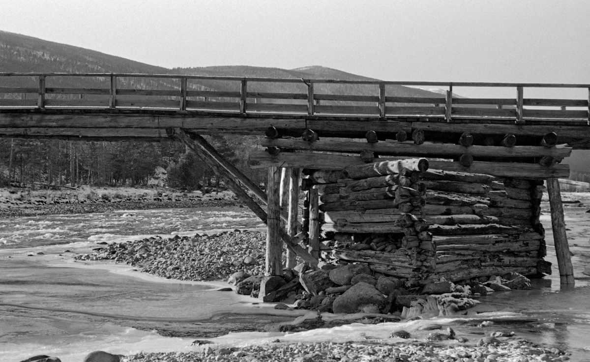 Detalj fra Ulekleivbrua over Gudbrandsdalslågen på Dovre, fotografert egn kald oktoberdag i 1955.  Dette var ei bjelkebru, bygd av tømmer.  For å kunne nå over det forholdsvis brede elvefaret med dette byggematerialet hadde man reist et brukar – ei steinfylt tømmekiste – på ei røys i elva, mellom landkarene på begge sider.  På denne tømmerkista hadde brubyggerne lagt ei rektangulær ramme med to omfar, som de øverste brubjelkene kvilte på.  Disse var også støttet av skråstivere fra det nevnte tømmerkistefundamentet og fra landkarene på begge sider.  Brua hadde trerekkverk. Trevirket i brukonstruksjonen virket temmelig værslitt da dette fotografiet ble tatt.