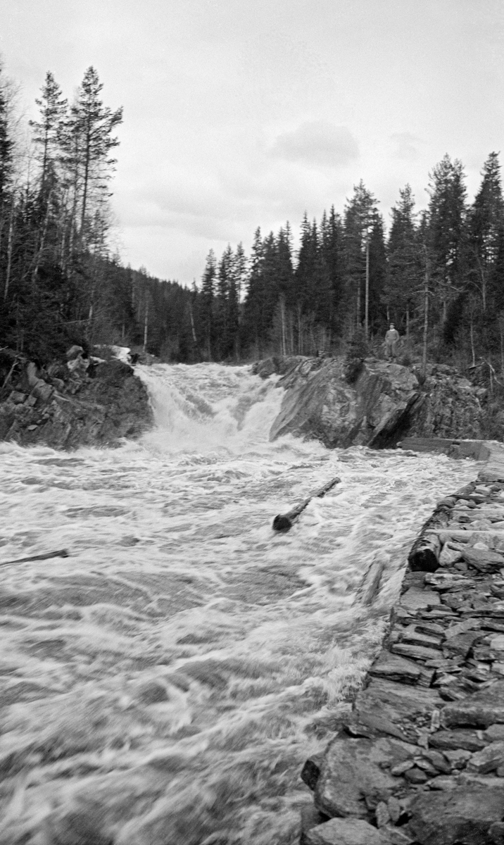 Fløting i ei elv som kalles Vala i Norderhov i Buskerud våren 1933.  Fotografiet er tatt fra en skådam av stein ved elvebredden, like nedenfor et fossefall.  Vi ser et par tømmerstokker i opprørt vann i forgrunnen.  Vi ser ellers at den nevnte skådammen hadde tømmerfront mot elveløpet litt ovenfor det stedet der fotografen tok bildet fra, at den ser ut til å være støpt, øverst, mot fossen.  På bergskrenten til høyre for fossen sto en mann og betraktet elva og tømmeret.  Bakenfor skimter vi høy barskog.