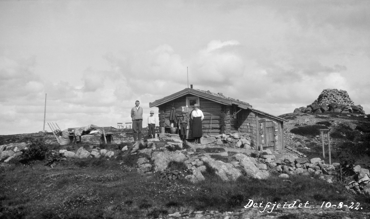 Deifjellet skogbrannvakstasjon i Åmot, Hedmark, fotografert 10. 8. 1922.  Deifjellet ligger i nærheten av Deset-grenda, og brannvaktstasjonen her ble etablert av Åmot brannvesen i 1898.  I første omgang ble det bare bygd ei enkel laftehytte på bakken.  Anlegget ble modernisert med økonomisk støtte fra forsikringsselskapet Skogbrand i 1932. 

Fotografiet viser den opprinnelige brannvakthytta, sett mot gavlveggen og inngangsdøra.  Det dreier seg om ei lav laftehytte med ett rom og inngang på gavlveggen.  Over inngangsdøra er det et lite, kvadratisk vindu.  Ved enden av den ene langveggen er det tilbygd et lite skur med pulttak i forlengelsen av brannvakthyttas saltak.  Dette skuret inneholdt antakelig vedbu og muligens utedo.  Foran brannvakthytta står en voksen mann og ei voksen kvinne med to barn mellom seg. De to til venstre er identifisert som skogeier Olav Mykleby (1877-1976) og hans eldste sønn Tollef Mykleby (1912-1987).  Kvinna ved husgavlen var sannsynligvis Tora Hedlund, som betjente denne brannvaktstasjonen i perioden 1922-1944. Vi ser også telefonstolpene med ledningen som skulle sikre rask varsling dersom det ble observert branntilløp fra stasjonen.  På et høydepunkt like bak hytta er det opplagt en diger, rund varde. 

De kommunale skogbrannreglene for Åmot er gjengitt under fanen «Opplysninger», se spesielt § 10.