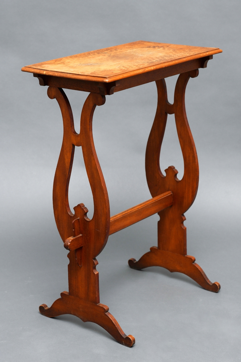 Et rektangulært bord i massiv treverk med to ben som har en halvsirkellignende utforming. En list nederst som binder de benene sammen.