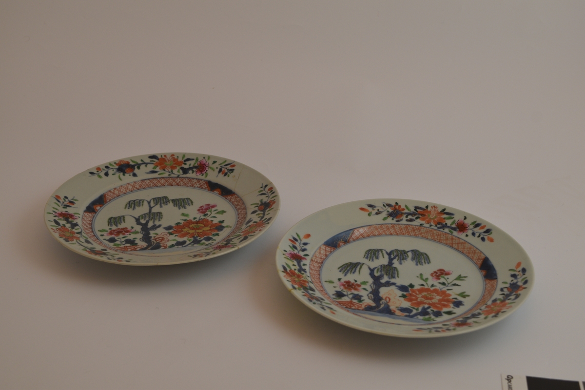 Runde porselensfat som er fargerikt dekorert med asiatisk inspirert motiv bestående av ett tre ved en elv med en bro over omringet av store mengder blomster. Dekoren består av mange farger men rød-orange dominer. Begge fatene er skadet og det ene har blitt reparert med tinn eller blylodding. Langs den indre "veggen" er det en 1,5 cm tykk stipe med rutete mønster.