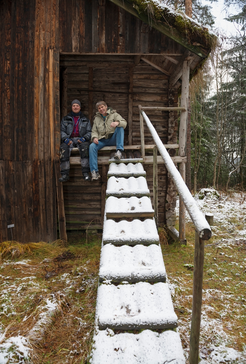 Tømrer Knut-Arild Nordli (til venstre) og konservator Bjørn Bækkelund i samtale om den antikvariske bebyggelsen i Norsk Skogmuseums friluftsmuseum på Prestøya i Elverum.  Karene sitter på kanten av ganggolvet foran mannskapsrommet i den toetasjes stallkoia («Flystua») fra Namdalen [SJF-B. 0008].  Hedmark fylkesmuseums forum for samlingsforvaltning engasjerte Knut-Arild Nordli våren 2012 for å få tilstandsvurdert de antikvariske bygningene i alle fylkesmuseets avdelinger.  Nordli tok sikte på å definere materialbehov og tidsforbruk knyttet til eventuelle restaureringstiltak på alle de cirka 500 antikvariske bygningene museet har ansvar for. Vurderingsarbeidet i Skogmuseets friluftsmuseum på Prestøya startet seinhøstes i 2012.  Ettersom det da var for kaldt til at takkonstruksjonene kunne undersøkes med blant annet fuktmålinger, ble dette arbeidet utsatt til 2013.  Tilstandsvurderinga av antikvariske bygninger i Hedmark fylkesmuseum planlegges videreført også i 2014. 