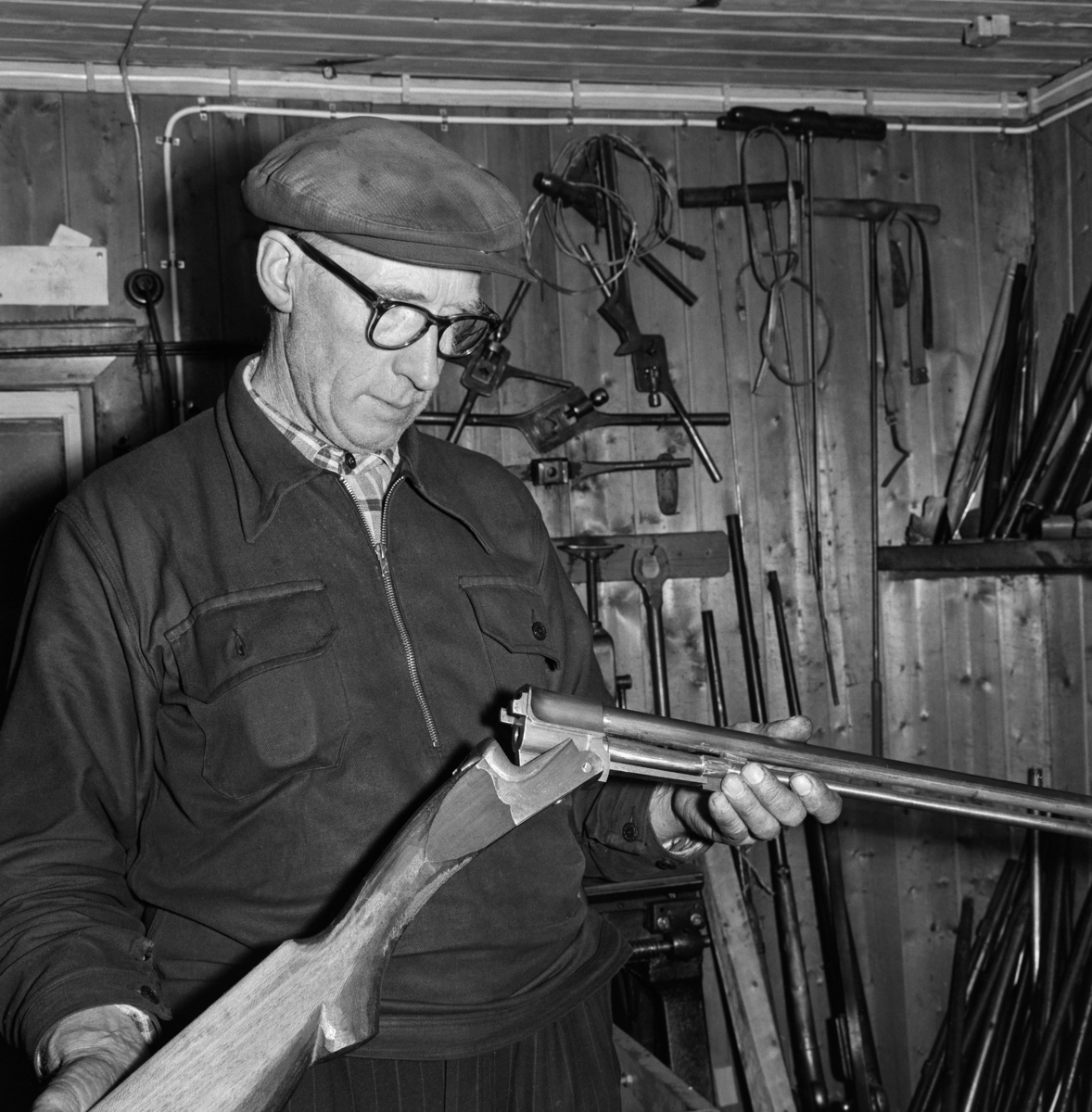 Børsemaker Karl Karlsen (1904-1995) fra Grue i Hedmark, fotografert i verkstedet sitt.  Børsemakeren står med et gevær i hendene.  Han var arbeidskledd, og hadde sixpencelue på hodet og hornbriller på nesa.  På veggen i bakgrunnen henger en del gjengeverktøy.  Nederst til høyre i bildeflata ser vi også pipene på en del geværer som er stilt mot veggen.  Bildet skal være tatt midt i 1960-åra. 

Litt informasjon om Karl Karlsen finnes under fanen «Opplysninger».