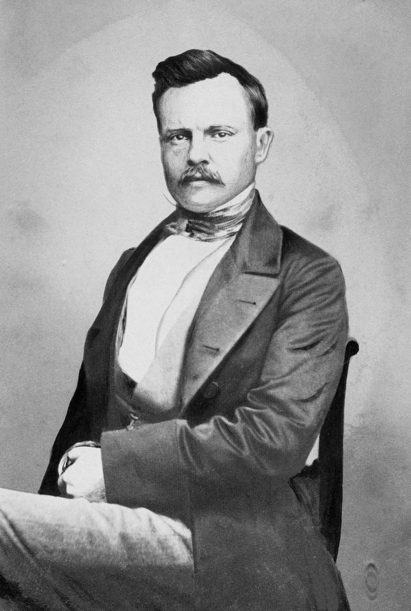 Fotografisk portrett av den tyske forstmannen Friederich Casimir Gustav Heyer (1826-1883), vanligvis bare omtalt som Gustav Heyer. Han er avbildet sittende på en stol i et fotografisk studio. Heyer var kledd i ei lang, frakkeliknende jakke med store slag, med vest og kvit skjorte under.  Om hanlsen har han knyttet et silketørkle. Da dette fotografiet ble tatt var den kjente forstmannen antakelig i 30-40-åra. Han hadde bart og skrått bakoverstrøket, mørkt hår.  

Gustav Heyer var sønn av Karl Heyer, som var professor ved det kjente skogakademiet i Giessen i den tyske delstaten Hessen.  Han gikk på gymnas i hjembyen, og etter at han hadde tatt artium satt han åtte semestre under (1843-1847) under farens kateter.  Deretter reiste den unge Gustav Heyer ut og praktiserte et par år, før han vendte tilbake til Giessen i 1849-1850.  Der var han først «privatdosent» en periode, inntil han i 1853 ble utnevnt til professor med forvaltningsansvar for skogene i området.  Med de erfaringene dette gav ham fikk han også undervisninsplikt i praktisk skogbehandling.  Gustav Heyer gjorde seg bemerket som en dyktig fagmann, og han skal ha blitt tilbudt professorater både i Zürich og Karlsruhe, tilbud han avslo, angivelig fordi han var så sterkt knyttet til hjemtraktene.  I 1868 sa han derimot ja til et tilbud om å bli direktør for det prøysiske forstakademiet i Münden, et embete som gav høyere lønn, samtidig som Heyer visste at forstinstituttet i Giessen var truet av omorganiseringer.  I 1875 skal han ha søkt et professorat ved den østerrikske «Hochschule für Bodenkultur», en stilling Heyer ikke fikk.  Etter dette bestemte han seg for å bli i Tyskland.  Som skogakademiker skal Gustav Heyer ha gjort seg bemerket med uvanlig bred naturfaglig innsikt, og som en klartenkt fagmann som visste å formidle sin faglige kompetanse så vel muntlig som skriftlig. Hans egen forskning var først og fremst knyttet til det skogøkonomiske fagfeltet, men han underviste og skrev også med suksess i mer produksjonsrelaterte emner som skogkultur og skognytting. 

En innrammet versjon av dette portrettet er registrert i Norsk Skogmuseums samling som gjenstand under nummeret SJF. 13546.