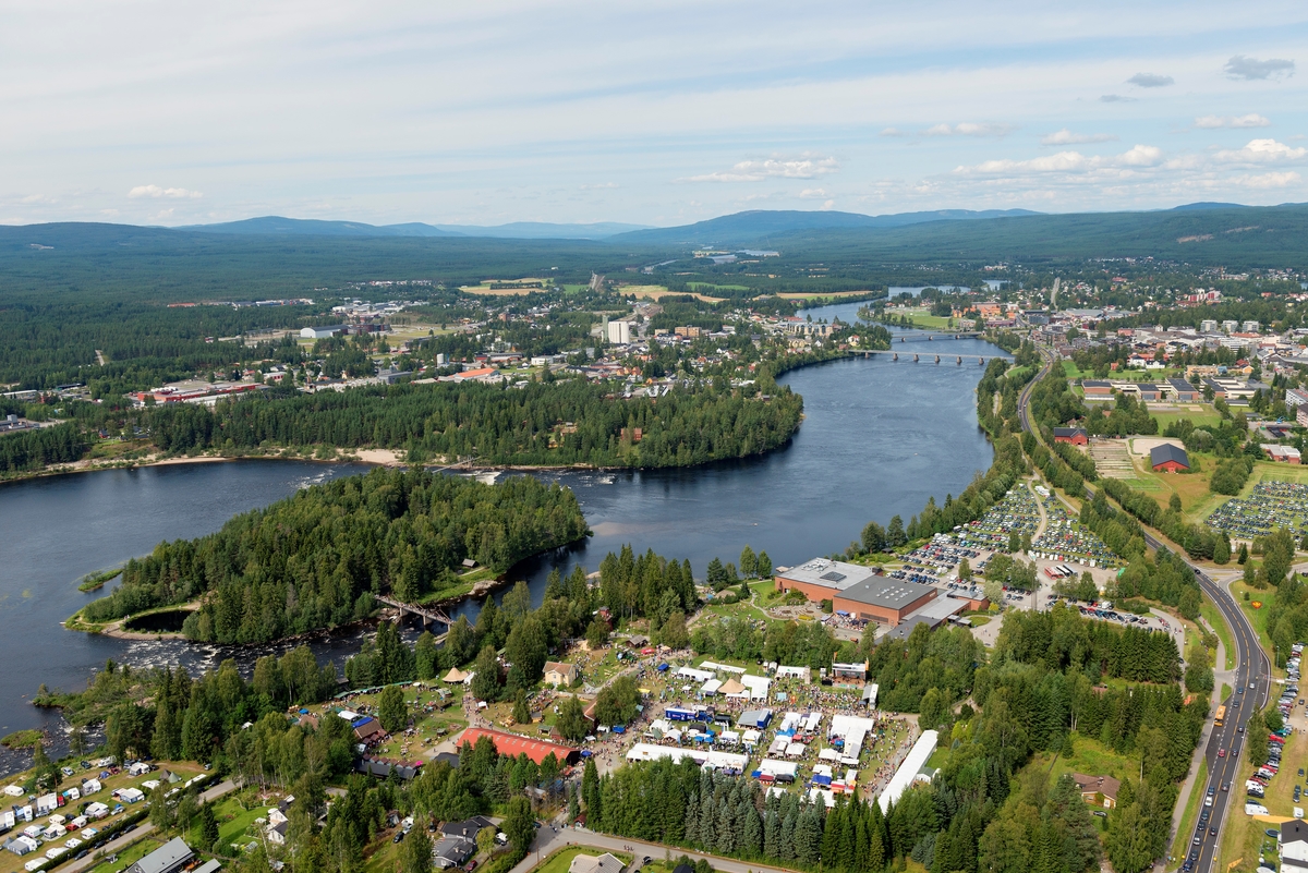 Norsk Skogmuseum i Elverum, sett fra lufta, 9. august 2014.  Fotografiet er tatt fra sør på lørdagen under De nordiske jakt- og fiskedager dette året, noe som preger aktiviteten på museet og i området omkring.  Museumsbygningene, to sammenbygde blokker på 40 X 40 meter, utført i betong med teglsteinsforblending, ligger litt til høyre og litt nedenfor midtpunktet i bildeflata.  På museets parkeringsplasser og på Nordjordet (arealet mellom museets nordgrense, Solørvegen og Glomma) samt på søndre del av Prestegardsjordet var det parkert store mengder biler.  Også campingplassen (nederst i venstre hjørne på fotografiet) var full.  Sør for museumsbygningene, på det som en gang var åkrene på klokkergarden Fossum, skimter vi utstillertelt og en masse mennesker.  Også i Norsk Skogmuseums friluftsmusem på Prestøya var det mye folk denne dagen, først og fremst på grunn av en jakthundutstilling med bortimot 700 påmeldte hunder.  På grunn av skogen på øye er ikke dette publikummet synlige på fotografiet.  På østsida av Glomma skimter vi deler av Elverum sentrum – Leiret – nord for Prestegarden.  På vestsida av ligger Glomdalsmuseets friluftsmuseum mot elva, sør for bydelen Vestad.  I bakgrunnen ser vi oppover mot Strandbygda. 

Den dagen dette fotografiet ble tatt var det 13 148 gjester som løste billetter til De nordiske jakt- og fiskedager.  I løpet av de fire dagene arrangementet pågikk var det 31 919 mennesker som besøkte museet. 