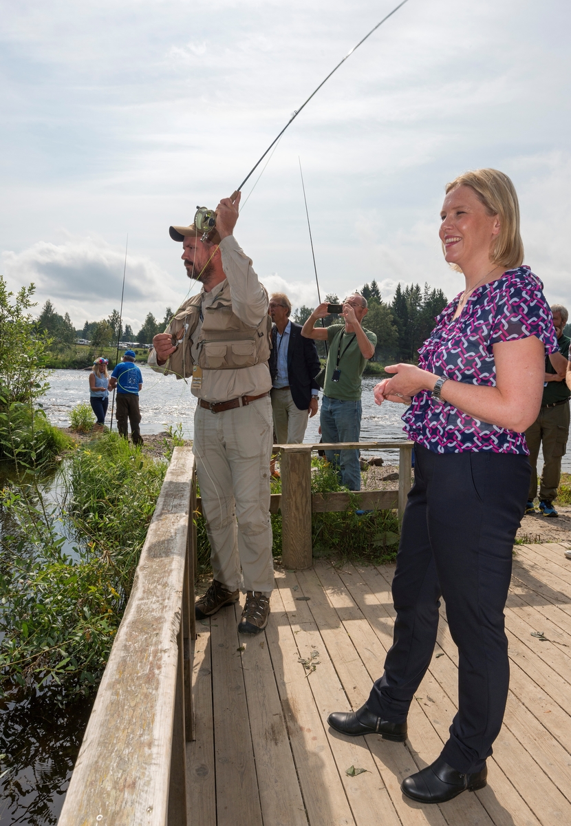 Fluefiskeren Tore Litleré Rydgren (til venstre) viser landbruks- og matminister Sylvi Listhaug fra Fremskrittspartiet fluefisketeknikk fra en plattform ved Norsk Skogmuseums fiskedam på Prestøya i Glomma.  Rydgren var kledd friluftsantrekk, blant annet med en vest med diverse fiskeutstyr på overkroppen.  Listhaug var kledd i mønstret, kortermet bluse og svart bukse.  Da dette fotografiet ble tatt hadde Rydgren overlatt fluestanga til gjesten, som etter hvert fanget en liten ørret.  Landbruks- og matministeren besøkte jakt- og fiskedagene som foredragsholder i seminaret «Gull og grønne skoger – nye grep for å øke skogens verdi og glede for alle» i museets auditorium.  Etterpå benyttet hun sjansen til å oppleve noe av programmet i museets friluftsmuseum, blant annet her ved fiskedammen. 