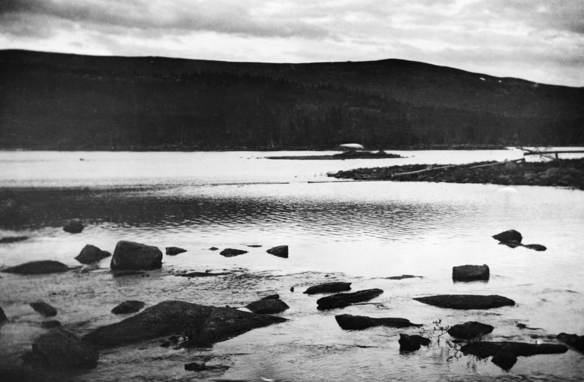 Mykletjønndammen i Austbygdåvassdraget i Tinn i Telemark.  Fotografiet er tatt var damsida (medstrøms) i en steinfylt tømmerkistedam, der veggene begynte å bli betydelig tæret av tidens tann.  Dammen hadde to åpninger, et lukeløp med fire stengslet til høyre og et noe mindre løp til venstre, som da fotografiet ble tatt sto uten noen form for stengsel.  Vi skimter fire mannsskikkelser på damkrona.  Dette var antakelig karer som var på befaring for å vurdere fornyingstiltak.  Det ble påbegynt ei ombygging av dette damanlegget i 1916, og dette bildet kan være tatt i samband med planlegginga av dette prosjektet. 

Mykletjønn ligger et par kilometer øst for Austbygdåe.  Denne lille innsjøen har avløp gjennom bekken Ordøla, som forener seg med vassdraget Lure før det når Austbygdåe.  Mykletjønn ligger 805 meter over havet, altså i et høydelag hvor det er lite tømmerskog.  Følgelig var det ikke ordinær fløting i Ordøla.  Mykletjønn var likevel regulert med en dam, som ble brukt til å holde et reservoar for fløtinga i hovedelva, Austbygdåa.  Den første dammen her må antakelig ha vært bygd på 1800-tallet, da firmaet S. & D. Cappelen på Gjemsøy ved Skien langt på veg var eneaktører i fløtinga i denne delen av Telemark.  Skiensvassdragets Fellesfløtningsforening bygde ny dam ved Mykletjønn i perioden 1916-1921. 