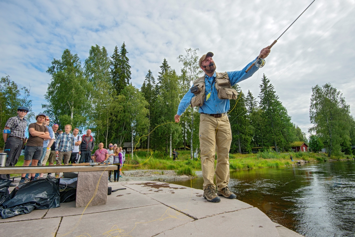 Tore Litleré Rydgren viser ulike kasteteknikker med fluestang for publikum under De nordiske jakt- og fiskedager på Norsk Skogmuseum i 2015.  Da dette fotografiet ble tatt sto Rydgren med fiskestanga ytterst på den granittutstikkeren som er lagd i Glomma som en del av museets og NVEs elvepark.  Rydgren hadde en mikrofon foran ansiktet, og bak ham sto ei interessert publikumsgruppe og forsøkte å tilegne seg noen av kasteteknikkene instruktøren kunne formidle.