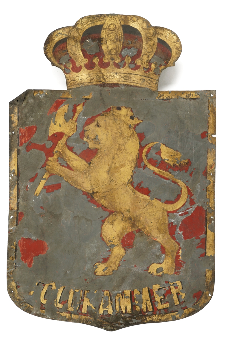 Firkantet metallskilt med avrundet kant nede ,med krone i gull og rødt over løve i gull med øks. Skiltet er rødt i bunnen med en kant i gull.Rikseplet med Olavskorset mangler på kronen. "TOLDKAMMER" er  skrevet i gull nederst på skiltet. Hull i alle hjørner fot antatt oppheng.