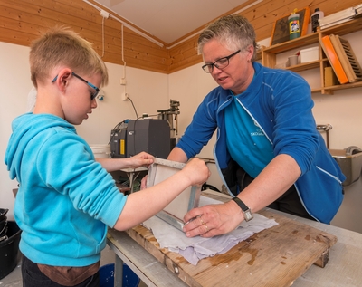 Fra det såkalte «papirkjøkkenet» ved Klevfos Industrimuseum på Ådalsbruk i Løten, Hedmark.  Da dette fotografiet ble tatt fikk en gutt fra 2. trinn ved Stavsberg skole i Furnes (Ringsaker kommune) hjelp av museumsformidler Trine Edvardsen til å lage sitt eget papirark.  Gutten overførte med stor forsiktighet fuktig papirmasse fra ei finmasket ramme til et underlag av filt, som etter hvert skal legges i press.  Ved Klevfos Industrimuseum håndlages papir som en introduksjon til hvordan papir framstilles i treforedlingsindustriens maskiner.  Pressinga med filtmellomlegg presenteres som en parallell til papirmaskinens pressparti.