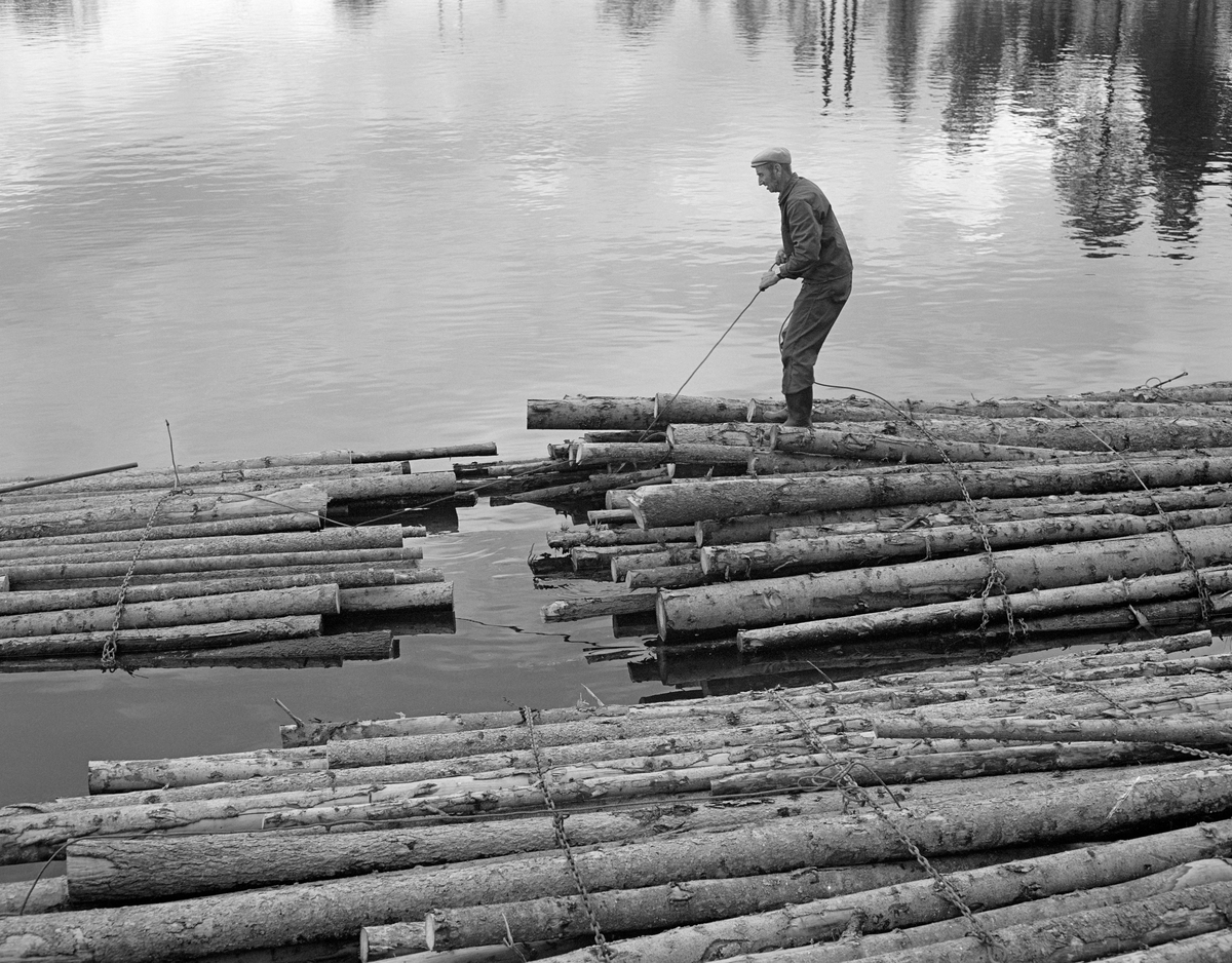 Tømmerfløteren Einar Melby (1915-2003) i arbeid på tømmerbunter - «moser» - ved Ørje sluser, der han hadde sin arbeidsplass gjennom mange år.  Mosene av ubarket massevirke, som var slått ut i vassdraget ved Skulerud litt lengre nord, skulle orienteres etter hverandre i korte lenker, såkalte «slusevendinger».  For å få dette til å bli stabilt dro Melby mosene inntil hverandre, ende mot ende.  Deretter trakk han et par stokker delvis ut av hver mose og delvis over i den tilstøtende, der de ble festet med kramper under et av vaierbindene som ble holdt mosen i hop. 

Det første sluseanlegget ved Ørje ble bygd i perioden 1857-1860, og fra 1877 ble tømmer fra de øvre delene av vassdraget fløtet ned til industrien i Halden på et kanalisert vassdrag.  En kort historikk om fløtinga i Haldenvassdraget finnes under fanen «Opplysninger».