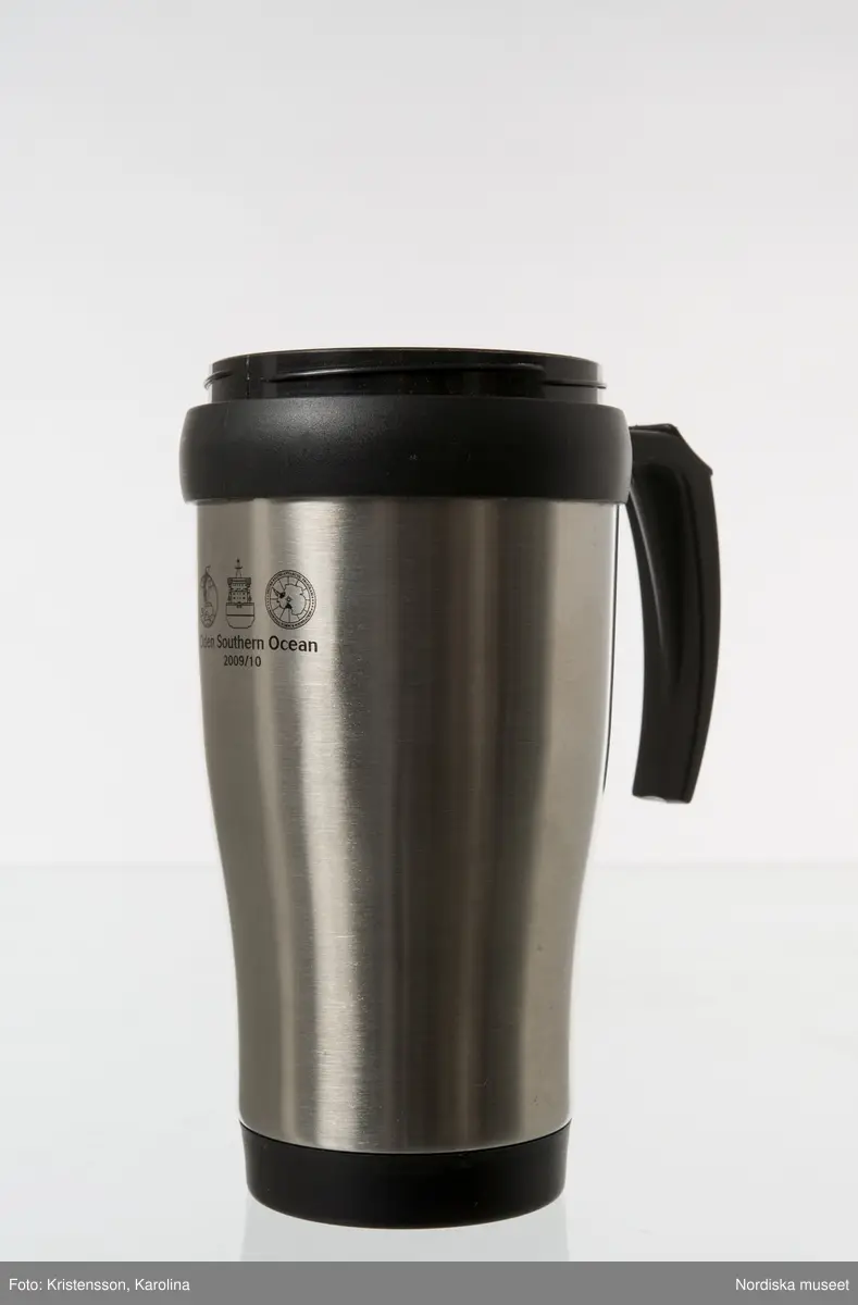 Termomugg av plast, med ytterhölje av aluminium. Används för varma drycker som kaffe och te. Locket saknas.