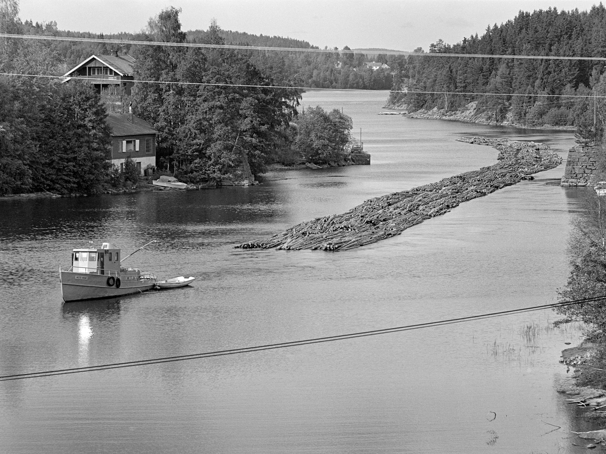 Slepebåten Mette Meng fotografert foran tømmerslep i Skotsbergelva i Aremark kommune i Østfold.  Dette er en cirka fire kilometer lang elvestrekning mellom Aremarksjøen (Ara) og Aspern.  Etter oppdemminga og kanaliseringa av vassdraget med dammer og sluseanlegg i Stenselva ved Krappeto og Brekke ligger de to nevnte sjøene om lag på samme høyde (105 meter over havet). Skotsbergelva er følgelig et forholdsvis stilleflytende elveløp hvor det var greit å slepe tømmer, sjøl om det var litt trangt i det partiet som kalles «Tordivelen».  Dette bildet ble tatt fra brua der riksveg 21 krysser vassdraget idet båten med tømmerslepet med tre lange lenker av tømmerbunter passerte Skotsberg brygge (ved vestre elvebredd, til venstre på bildet) like nord for brua.

En liten historikk om tømmerfløting og kanaliseringsarbeid i Haldenvassdraget finnes under fanen «Opplysninger».