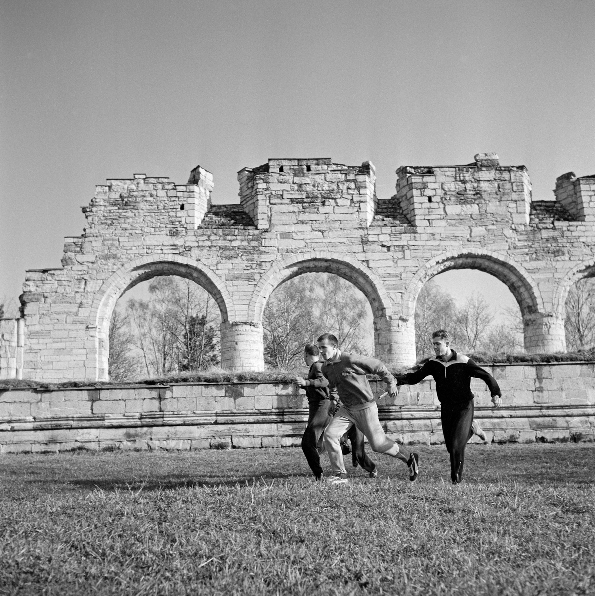 Veksling under Hamarstafetten 16. mai 1963.  Fotografiet er tatt på nordsida av Domkirkeruinen, der to lag vekslet med ruinen som bakgrunn.  Stafetten ble arrangert i samarbeid mellom Hamar Idrettslag og avisa Hamar Stiftstidende.  Løpet hadde ti etapper med vekslende lengde – fra 360 til 1 650 meter – med start og innkomst på Domkirkeodden etter en runde i gatene i bydelen Storhamar.  Konkurransen hadde tre klasser (klasse 1, klasse 2 og junior) og premiebordet ble ansett for å være meget attraktivt.