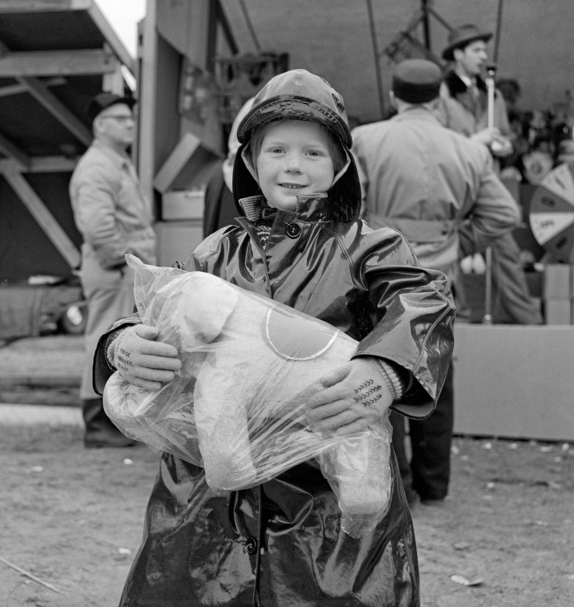 Fra Grundsetmart'n i kommunesenteret Leiret i Elverum i mars 1959.  Fotografiet viser et fornøyd barn, muligens en gutt, med en plastpakket elefant han nettopp hadde vunnet.  Barnet var kledd i svart regnfakk og hadde sydvest i samme materiale på hodet, noe som nok kunne komme vel med, for i 1959 regnet det stadig under mart'n.  I bakgrunnen skimter vi ei scene, der en mann med hatt på hodet sto framfor et mikrofonstativ.  Ved siden av denne mannen skimter vi deler av et lykkehjul.