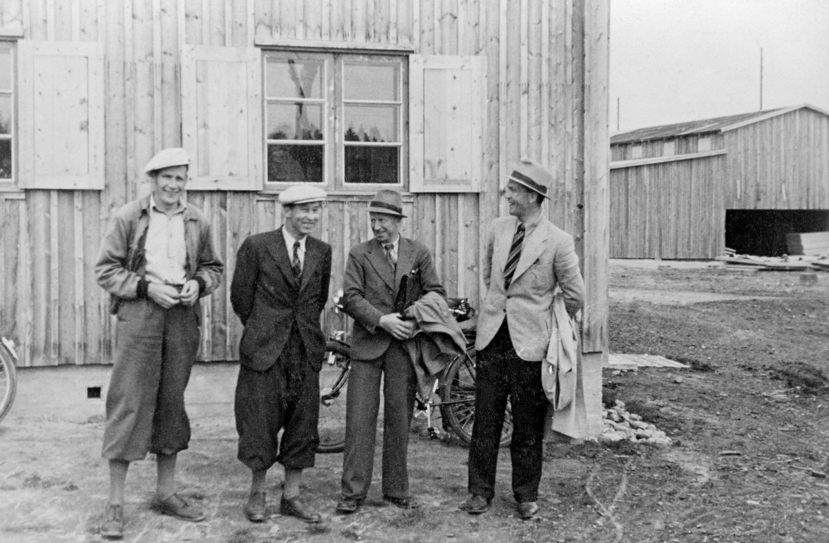 Fire menn, fotografert utenfor en av bygningene ved Våler skurlag på Braskereidfoss i Solør.  Fra venstre står Kåre Urdahl (1910-1989), Ottar Elseth (1901-1975) og Gustav Knøsen (1904-1980).  Mannen ytterst til høyre har vi foreløpig ikke navnet til.  Urdahl og Elseth satt i styret for det selskapet Vaaler felleslag (seinere kalt Våler skogeierlag) organiserte i 1939 for å overta driften av Våler kommunale sag og høvleri, som hadde vært i drift siden 1919.  Knøsen ble valgt inn i det samme styret i 1942.  Bildet er tatt framfor virksomhetens kontorbygning, som ble bygd like etter at det nye selskapet, Våler skurlag S/L. overtok virksomheten.  Kontorbygningen sto på en grunnmur av betong og med prefabrikerte veggelementer med tre lag panel og to lag isolerende papp.  Den hadde ei grunnflate på snaut 60 kvadratmeter og inneholdt tre rom.  Kontorbygningen fra 1939-40 ble erstattet av en større og med moderne administrasjonsbygning i Våler skurlags store ekspansjonsfase i slutten av 1960-åra. Til høyre i bildet ser vi brukets materialhus grunnflate på 815 kvadratmeter og men gjennomkjøring langs midtaksen.