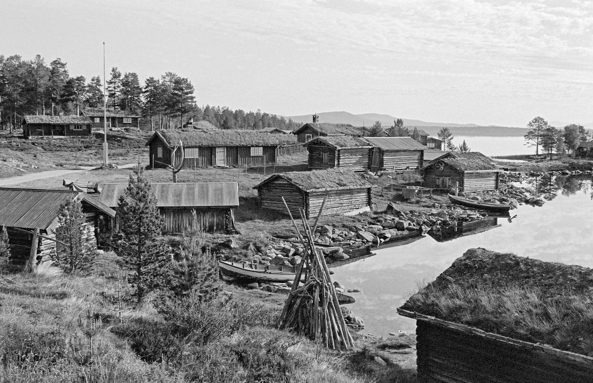 Fiskevollen ved Sølensjøen i Øvre Rendalen slik stedet så ut i 1983.  Fotografiet viser noe av den gjenværende bebyggelsen på dette innlandsfiskeværet.  Sølensjøen ligger snaut 700 meter over havet og cirka tre mil øst for de gardene i Øvre Rendalen hovedbygd som ha har fiskerettigheter i sjøen.  Inntil det i perioden 1939-1941 ble bygd bilveg på denne strekningen, foregikk transporten til og fra sjøen med kløvhester på barmark og på sleder vinterstid.  Lange avstander og tidkrevende transportmetoder gjorde det nødvendig å etablere et bygningsmiljø ved sjøen for innkvartering av fiskere, oppbevaring av båter, redskaper og fisk.  Det viktigste fisket foregikk i den søndre delen av sjøen, men der lå fjellmassivet Sølen en barriere mot bygda.  Fra Fiskevollen ved den nordvestre delen av sjøen derimot, var det greit farbart terreng vestover mot bygda.  Fiskeværet lå i ei lun vik hvor fiskebåtene kunne ligge skjermet for vind, og hvor husene kunne plasseres noenlunde lunt til i terrenget.  Fiskerne bodde på Fiskevollen under sommerfisket.  Under høstfisket etter røye sør i sjøen bodde fiskerne i fire felleseide buer i nærheten av gytegrunnene.  Fiskefangstene ble imidlertid rodd opp til Fiskevollen, hvor de ble lagret inntil de kunne kjøres til bygds på sledeføre.  Det var tre bygningstyper på Fiskevollen: Naustene, som la nede i strandsonen, buene fiskerne bodde i og kjellene de oppbevarte fiskeutstyret i høyere oppe på strandbakken.  I nyere tid har en del av buene fått mer hyttepreg.  I 1980 var det 59 bygninger på Fiskevollen.  Dette fotografiet viser den sentrale delen av innlandsfiskeværet, sett fra sør mot nord.  Et par båter lå ved stranda da bildet ble tatt.