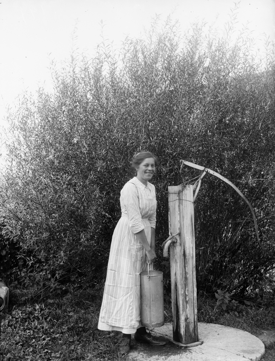 Hildegard Pettersson vid vattenpump på Alinders gård, Sävasta, Altuna socken, Uppland i början av 1900-talet