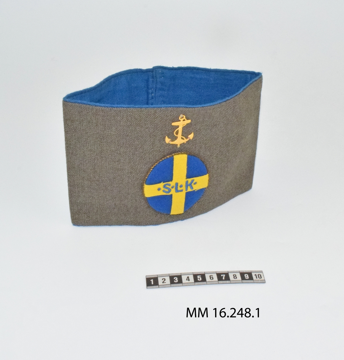 Armbindel för marinlotta. Rektangulärt tygstycke, dubbelt. Framstycket gråbrungrönt, bakstycket mellanblått. Bakstycket bildar blå passpoal runt det gråbrungröna stycket. I mitten på framstycket cirkelrunt emblem i tyg: Riksförbundet Sveriges lottakår: blå botten, gult kors med broderade bokstäver, blå: " . S . L . K .". Lagd gul metallpåsytt. Ovan emblemet gul metallankare fastsytt: flottans emblem.

:1 ihopsydd i kortändarna.