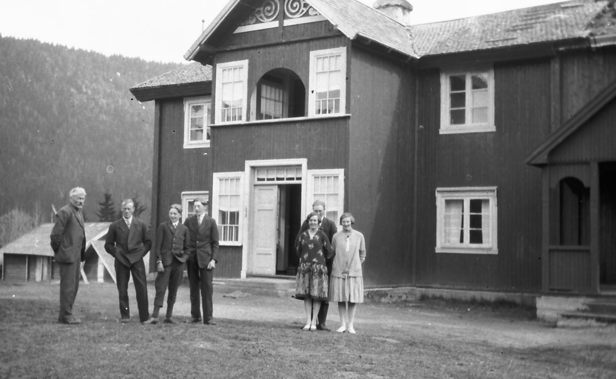 Folk foran hus med veranda som har vinduer (byggeskikk). 