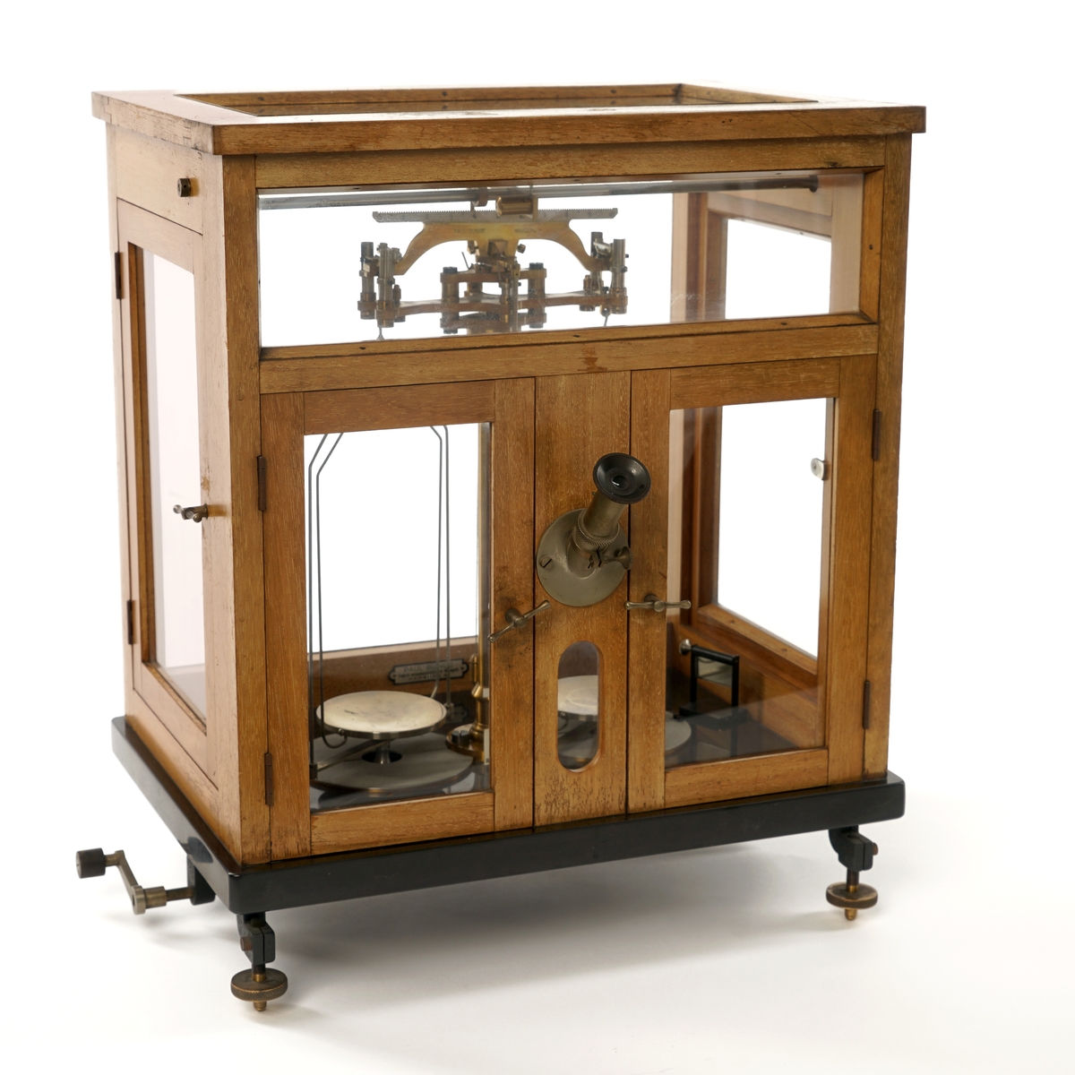 Vekt montert inn i et  monter med to dører i front og en dør på hver side. Monteret har et  "skjellet" i tre  og hvor alle sider og tak er innglasset. I fronten  er det også montert et mikroskop. På venstre side er det festet en justeringssveiv.
Under på baksiden er det skrudd fast en fot, på forsiden er det festet to justerbare føtter. Inne i monteret er det et løst speil. Alle dører har en lukkemekanisme i metall. Gulvet er antatt sort granitt. Øverst til høyre i monteren er det montert en justeringsskrue.