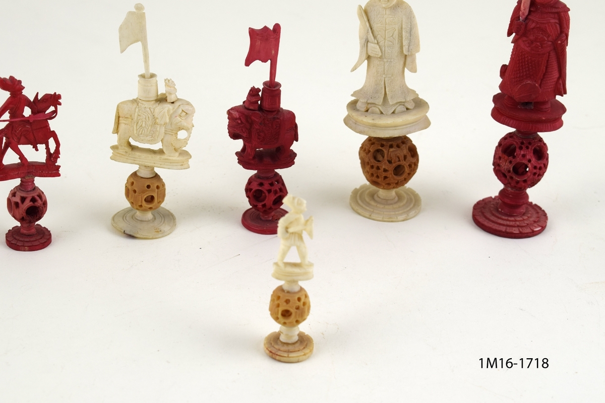 Röda och vita shackpjäser. Totalt 32 figurer. Figurerna i form av människor och elefanter. Minsta figuren 6cm. Största figuren 13 cm.