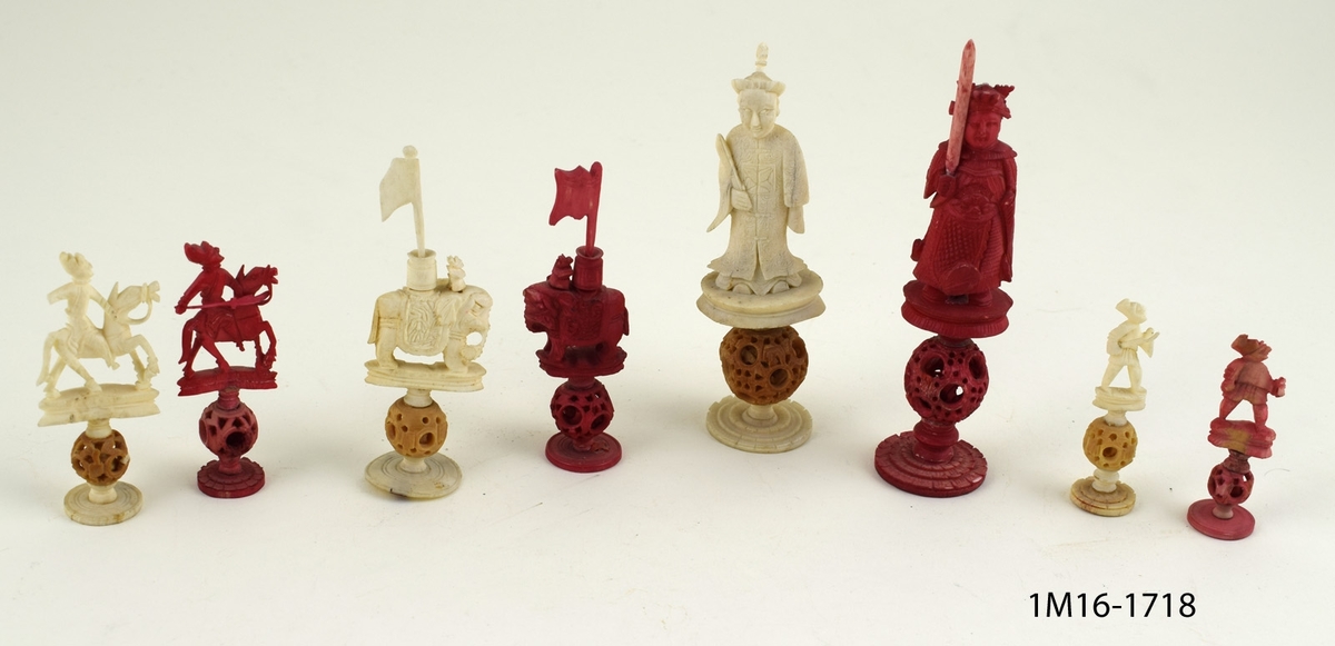 Röda och vita shackpjäser. Totalt 32 figurer. Figurerna i form av människor och elefanter. Minsta figuren 6cm. Största figuren 13 cm.