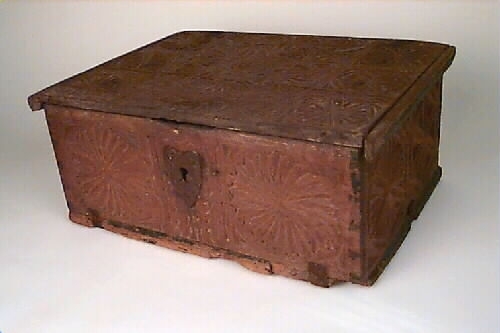 Skrin med fällock på smidda gångjärn. Hjärtformad nyckelskylt i järn. Låset borttaget. Botten fäst med metallbeslag. Skrinet är dekorerat med heltäckande karvsnittsdekor. På locket en stor och sex små karvsnittsrosetter. Även på sidorna karvsnittsrosetter. Alla olika. På locket vid låset bokstäverna "BSDS". Skrinet har troligen från början haft kulfötter i hörnen. Skrinet är bemålat inuti. I skrinet rött och i locket gult. Färgrester även på utsidan. 