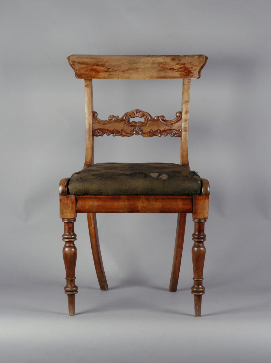 Biedermeier. Antatt bjørk med mahognybeis. Rett, noe tilbakeoverlenet, åpen rygg med utskåret midtsprosse. Det øvre tverrbrettet er glatt, noe svunget, og avrundet i hjørnene. Ingen armlener. Dreide, rette forben, lett bakoversvungne firkantede bakben. Stoppede seter, trukket med bomullsdamask. To av stolene trukket med sort trekk, to med mørkegrønt trekk.