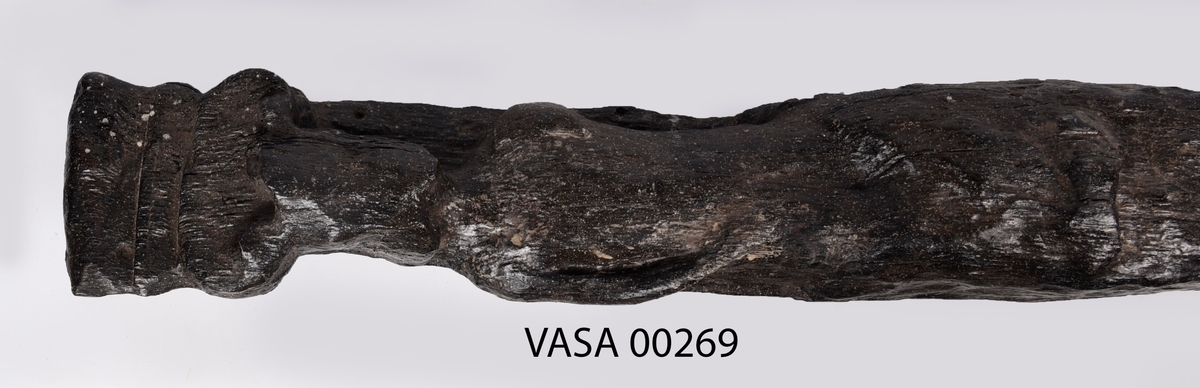 Skulpterad pilaster föreställande en herm eller möjligtvis en karyatid, under jonisk kapitäl.
Huvudet är vridet åt vänster samt prytt med en krona. Armarna hålls sträckta utefter sidorna.
Kroppen övergår i det med blad- och blomornamentik rikt sirade pilasterskaftet som smalnar av nedåt. Skaftet avgränsas genom en enkel vulst eller list från den rikt sirade och mjukt utbuktande piedestalen. Nedtill är piedestalen försedd med en bred bas. Skulpturens baksidan är slät.
Skulpturen är sliten.

Text in English: Sculptered pilaster with a Herm, or possibly a Caryatid, beneath an Ionic capital.
The head, with a crown, is turned to the left. The arms are streched out along the sides.
The body extends into the shaft of the pilaster, which tapers downwards and is richly decorated with leaf and flower ornamentation. A simple torus or batten separates the shaft from the richly decorated, softly bulging pedestal that has a broad base. The back of the sculpture is smooth.
The sculpture is worn.