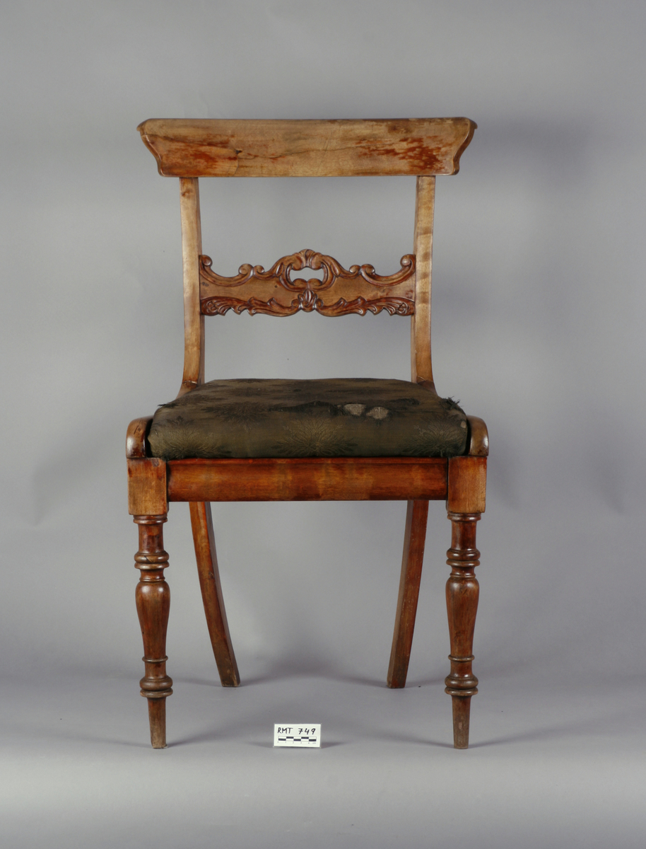 Biedermeier. Antatt bjørk med mahognybeis. Rett, noe tilbakeoverlenet, åpen rygg med utskåret midtsprosse. Det øvre tverrbrettet er glatt, noe svunget, og avrundet i hjørnene. Ingen armlener. Dreide, rette forben, lett bakoversvungne firkantede bakben. Stoppede seter, trukket med bomullsdamask. To av stolene trukket med sort trekk, to med mørkegrønt trekk.