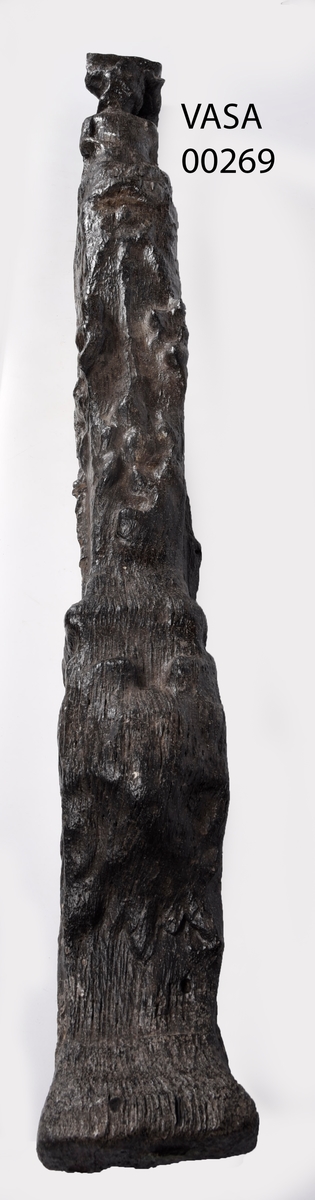 Skulpterad pilaster föreställande en herm eller möjligtvis en karyatid, under jonisk kapitäl.
Huvudet är vridet åt vänster samt prytt med en krona. Armarna hålls sträckta utefter sidorna.
Kroppen övergår i det med blad- och blomornamentik rikt sirade pilasterskaftet som smalnar av nedåt. Skaftet avgränsas genom en enkel vulst eller list från den rikt sirade och mjukt utbuktande piedestalen. Nedtill är piedestalen försedd med en bred bas. Skulpturens baksidan är slät.
Skulpturen är sliten.

Text in English: Sculptered pilaster with a Herm, or possibly a Caryatid, beneath an Ionic capital.
The head, with a crown, is turned to the left. The arms are streched out along the sides.
The body extends into the shaft of the pilaster, which tapers downwards and is richly decorated with leaf and flower ornamentation. A simple torus or batten separates the shaft from the richly decorated, softly bulging pedestal that has a broad base. The back of the sculpture is smooth.
The sculpture is worn.