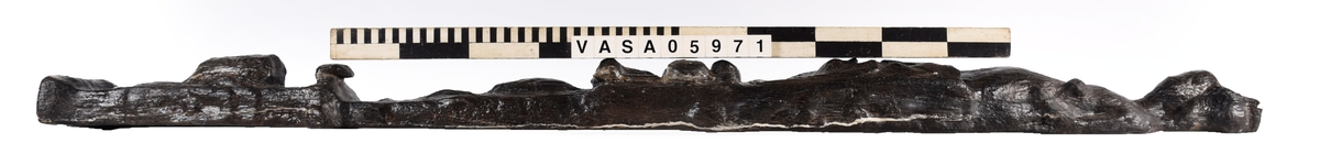 Skulpterad pilaster utformad som en karyatid med långt hår, troligen placerad under ett joniskt kapitäl.
Huvudet är vridet åt vänster. Höger arm är sträckt utefter sidan. Vänster arm är böjd och i handen håller figuren ett okänt föremål.
Pilasterskaftet är upptill prytt med en maskaron med bred, öppen mun och nedtill med en tung fruktfeston. Det nedåt avsmalnande pilasterskaftet avgränsas från piedestalen av en enkel vulst eller list med uppdragna kanter. Piedestalen är hög och jämnbred samt prydd med ett litet huvud och avslutas nedtill med en förtjockad bas. Skulpturens baksida är slät.
Skulpturen är kraftigt sliten och nött med finare detaljer utplånade.

Text in English: Sculpted pilaster with Caryatid with long hair under what is possibly an Ionic capital.
The head is turned to the left, the right arm is streched along the side, the left arm is bent and the hand holds an unknown object.
The shaft of the pilaster is decorated above with a mask with a broad, open mouth, below is a heavy festoon of fruit. The shaft tapers downwards and is divided from its pedestal by a simple torus or batten with drawn-up edges. The pedestal is high and even in width and decorated with a small head. It terminates at the bottom in a thickened base. Its back is smooth.
The sculpture is much worn, with finer details obliterated.