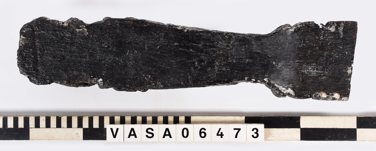 Liten skulpterad pilaster, utformad som en karyatid eller möjligen en putto. Figuren har långt hår och ett knubbigt ansikte, omgivet av en bred krage. Pilasterskaftet är dekorerat med akantusblad. Nedtill avslutas pilastern av en rikt profilerad och dekorerad sockel. Skulpturens baksida är slät.
Skulpturen är mycket sliten.

Text in English: A small carved pilaster, with a caryatid or probably a putto. The figure has a chubby face, long hair and a broad collar. The lower part of the pilaster is decorated with acanthus leaves. The figure stands on a richly profiled and decorated socle. The back of the sculpture is smooth.
The sculpture is very worn.