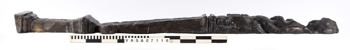 Skulpterad pilaster med övre delen i form av en karyatid med yppig, konstrik frisyr.
Höger arm hålls böjd med handen placerad framför bröstet. Vänster arm hålls utsträckt utefter sidan med handen vilande mot höften. Underkroppen döljs av ett hölje som framtill är prytt med stora, spiralformade ornament och små djurfigurer.
Karyatiden avgränsas från det rullverksornerade pilasterskaftet av en profilerad list. Nedtill avslutas skaftet av ett rullverksornament ovanför den rikt profilerade basen. Nedtill är pilastern försedd med en hög piedestal, prydd med beslagsornamentik. Figuren och dekoren omfattar även pilasterns sidor. Baksidan är slät.


Text in English: Sculpted pilaster with its upper part shaped as a Caryatid with a luxuriant artistic coiffure.
The right arm is held bent with the hand in front of the breast, the left arm is held at the side with the hand resting against the thigh. The lower part of the body is concealed by a shift or slip that is decorated with large spiral-shaped ornaments and small figures of animals.
A profiled batten separates the Caryatid from the shaft of the pilaster, which is ornamented with scrollwork. The shaft terminates with a scrollwork ornament above the richly profiled base. Below, the pilster is equipped with a high pedestal, decked with applied ornamentation. The back is smooth.