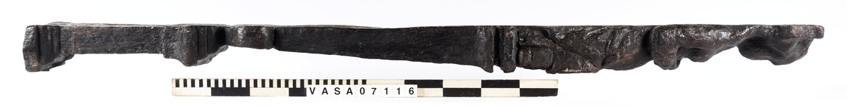 Skulpterad pilaster med övre delen i form av en karyatid med yppig, konstrik frisyr.
Höger arm hålls böjd med handen placerad framför bröstet. Vänster arm hålls utsträckt utefter sidan med handen vilande mot höften. Underkroppen döljs av ett hölje som framtill är prytt med stora, spiralformade ornament och små djurfigurer.
Karyatiden avgränsas från det rullverksornerade pilasterskaftet av en profilerad list. Nedtill avslutas skaftet av ett rullverksornament ovanför den rikt profilerade basen. Nedtill är pilastern försedd med en hög piedestal, prydd med beslagsornamentik. Figuren och dekoren omfattar även pilasterns sidor. Baksidan är slät.


Text in English: Sculpted pilaster with its upper part shaped as a Caryatid with a luxuriant artistic coiffure.
The right arm is held bent with the hand in front of the breast, the left arm is held at the side with the hand resting against the thigh. The lower part of the body is concealed by a shift or slip that is decorated with large spiral-shaped ornaments and small figures of animals.
A profiled batten separates the Caryatid from the shaft of the pilaster, which is ornamented with scrollwork. The shaft terminates with a scrollwork ornament above the richly profiled base. Below, the pilster is equipped with a high pedestal, decked with applied ornamentation. The back is smooth.