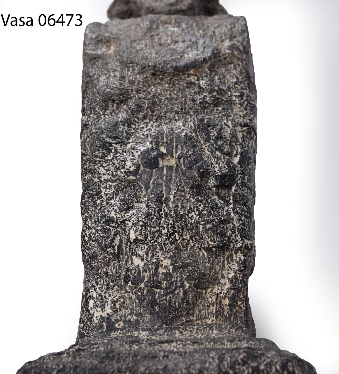Liten skulpterad pilaster, utformad som en karyatid eller möjligen en putto. Figuren har långt hår och ett knubbigt ansikte, omgivet av en bred krage. Pilasterskaftet är dekorerat med akantusblad. Nedtill avslutas pilastern av en rikt profilerad och dekorerad sockel. Skulpturens baksida är slät.
Skulpturen är mycket sliten.

Text in English: A small carved pilaster, with a caryatid or probably a putto. The figure has a chubby face, long hair and a broad collar. The lower part of the pilaster is decorated with acanthus leaves. The figure stands on a richly profiled and decorated socle. The back of the sculpture is smooth.
The sculpture is very worn.