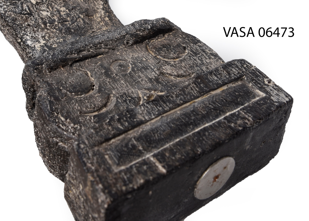 Liten skulpterad pilaster, utformad som en karyatid eller möjligen en putto. Figuren har långt hår och ett knubbigt ansikte, omgivet av en bred krage. Pilasterskaftet är dekorerat med akantusblad. Nedtill avslutas pilastern av en rikt profilerad och dekorerad sockel. Skulpturens baksida är slät.
Skulpturen är mycket sliten.

Text in English: A small carved pilaster, with a caryatid or probably a putto. The figure has a chubby face, long hair and a broad collar. The lower part of the pilaster is decorated with acanthus leaves. The figure stands on a richly profiled and decorated socle. The back of the sculpture is smooth.
The sculpture is very worn.