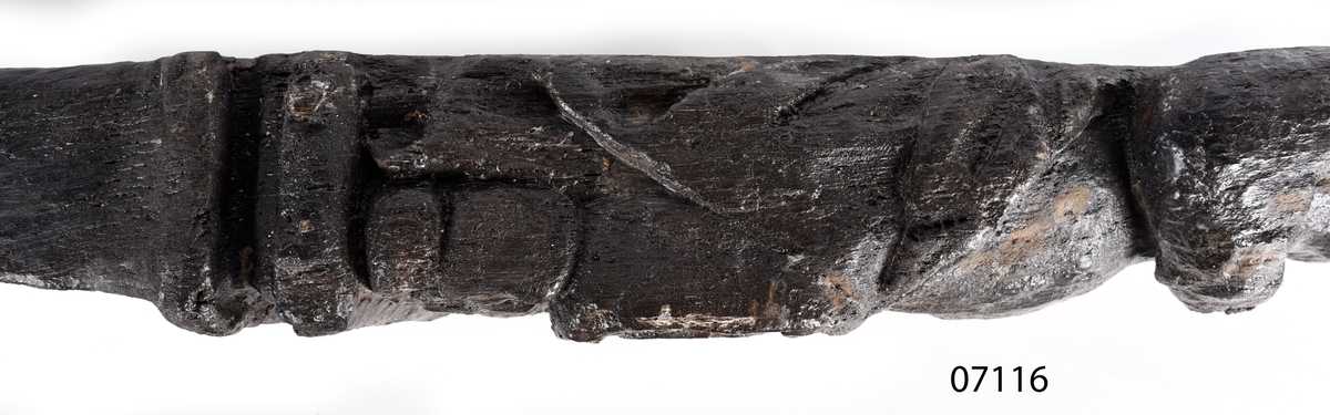 Skulpterad pilaster med övre delen i form av en karyatid med yppig, konstrik frisyr.
Höger arm hålls böjd med handen placerad framför bröstet. Vänster arm hålls utsträckt utefter sidan med handen vilande mot höften. Underkroppen döljs av ett hölje som framtill är prytt med stora, spiralformade ornament och små djurfigurer.
Karyatiden avgränsas från det rullverksornerade pilasterskaftet av en profilerad list. Nedtill avslutas skaftet av ett rullverksornament ovanför den rikt profilerade basen. Nedtill är pilastern försedd med en hög piedestal, prydd med beslagsornamentik. Figuren och dekoren omfattar även pilasterns sidor. Baksidan är slät.


Text in English: Sculpted pilaster with its upper part shaped as a Caryatid with a luxuriant artistic coiffure.
The right arm is held bent with the hand in front of the breast, the left arm is held at the side with the hand resting against the thigh. The lower part of the body is concealed by a shift or slip that is decorated with large spiral-shaped ornaments and small figures of animals.
A profiled batten separates the Caryatid from the shaft of the pilaster, which is ornamented with scrollwork. The shaft terminates with a scrollwork ornament above the richly profiled base. Below, the pilster is equipped with a high pedestal, decked with applied ornamentation. The back is smooth.