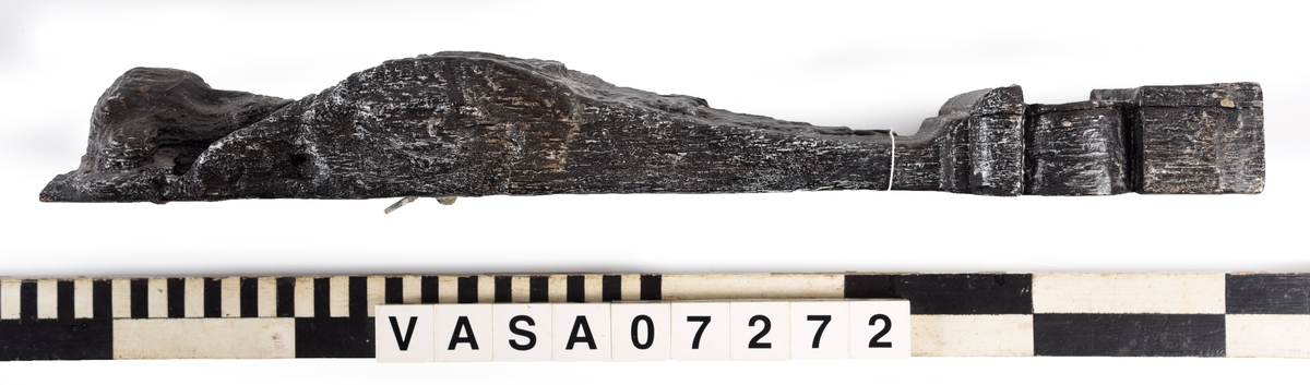 Liten skulpterad pilaster, utformad som en karyatid eller möjligen en putto. Figuren har långt hår och ett knubbigt ansikte, omgivet av en bred krage. Det nedåt avsmalnande pilasterskaftet är dekorerat med akantusblad. Nedtill avslutas pilastern av en rikt profilerad och dekorerad sockel. På skulpturens släta baksida sitter en nygjord upphängningsanordning, fästad med två skruvar.
Skulpturen är sliten.

Text in English: A small carved pilaster, with a caryatid or probably a putto. The figure has a chubby face, long hair and a broad collar. The lower part of the pilaster is decorated with acanthus leaves. The caryatid stands on a richly profiled and decorated socle. On the smooth back of the sculpture is a new hanging device attached with two screws.
The sculpture is worn.